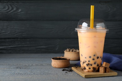 Photo of Tasty brown milk bubble tea in plastic cup on light blue wooden table. Space for text