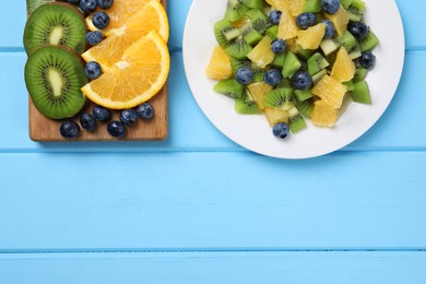 Photo of Plate of tasty fruit salad and ingredients on light blue wooden table, flat lay. Space for text