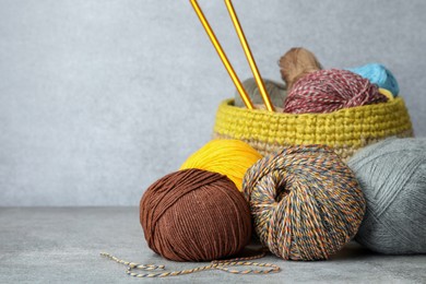 Photo of Soft woolen yarns and knitting needles on grey table, space for text