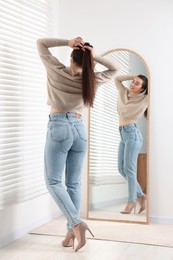 Young woman in stylish jeans near mirror indoors