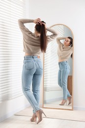 Photo of Young woman in stylish jeans near mirror indoors