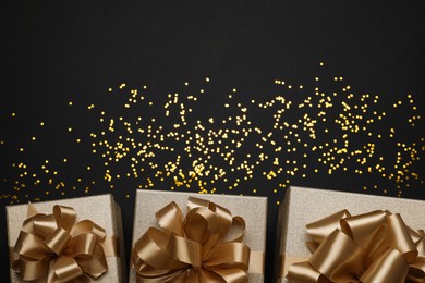 Golden gift boxes and confetti on black background, flat lay. Space for text