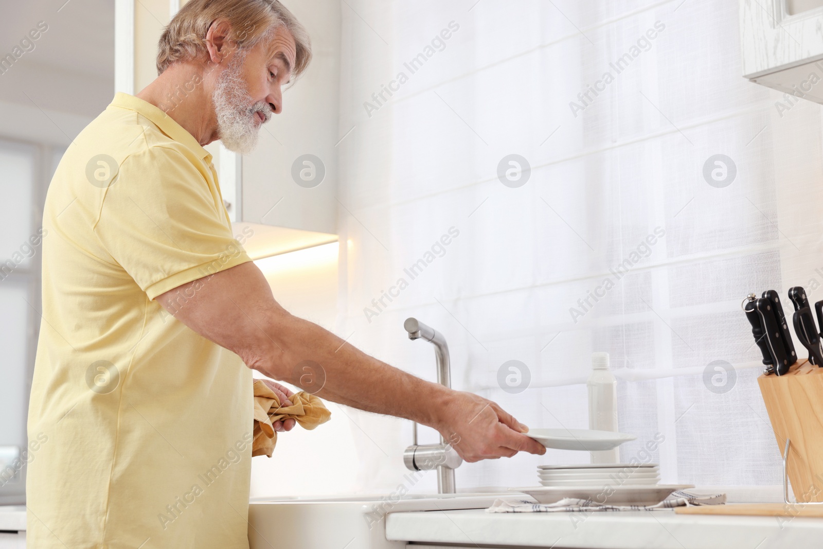 Photo of Senior man putting plate on stack of ones in kitchen, space for text