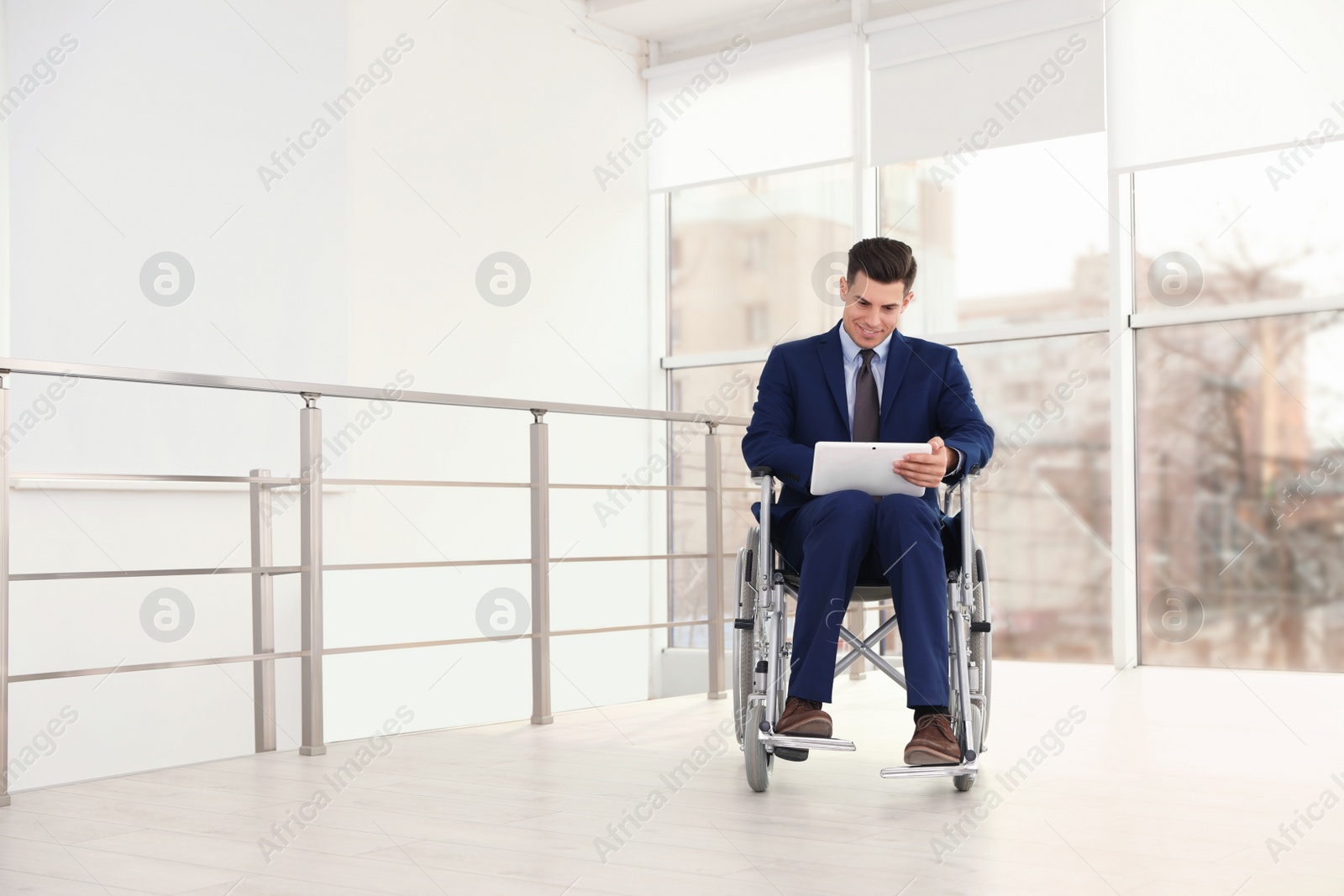 Photo of Young businessman in wheelchair using tablet near window indoors