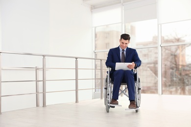 Photo of Young businessman in wheelchair using tablet near window indoors