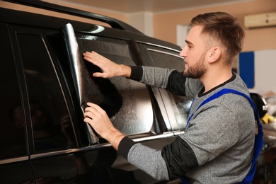 Worker tinting car window with foil in shop