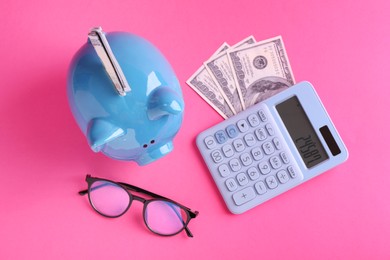 Photo of Financial savings. Piggy bank, dollar banknotes, glasses and calculator on pink background, flat lay