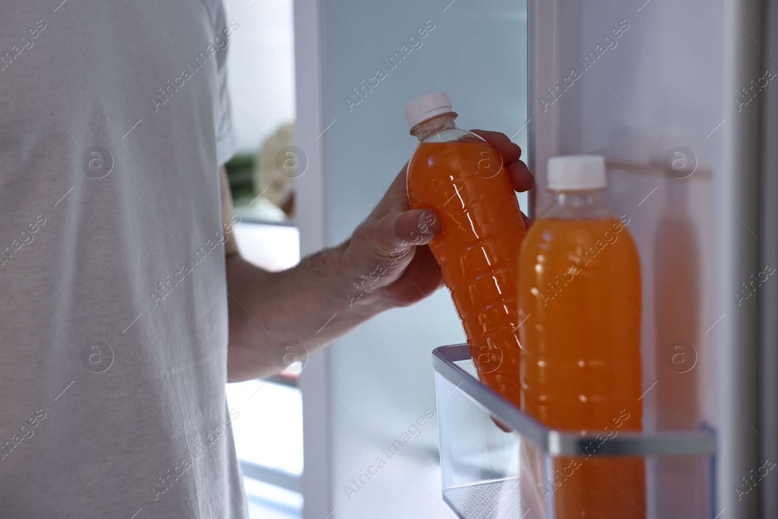 Photo of Man taking bottle of juice out of refrigerator at night, closeup