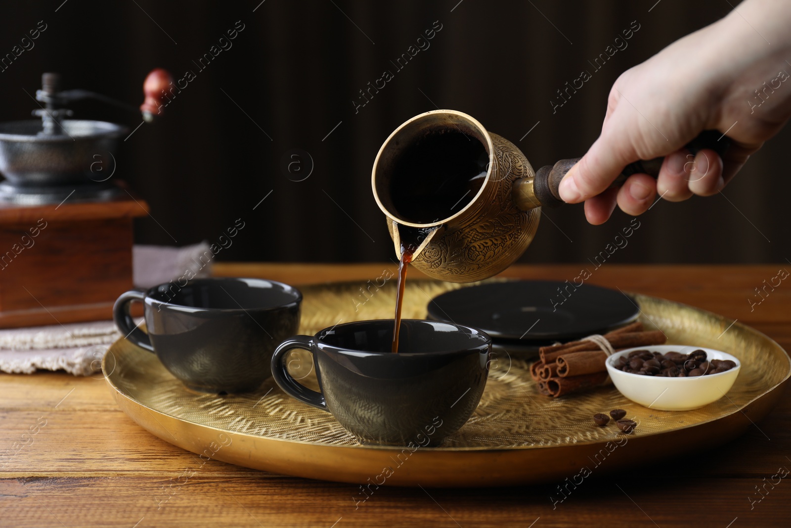 Photo of Turkish coffee. Woman pouring brewed beverage from cezve into cup at wooden table, closeup