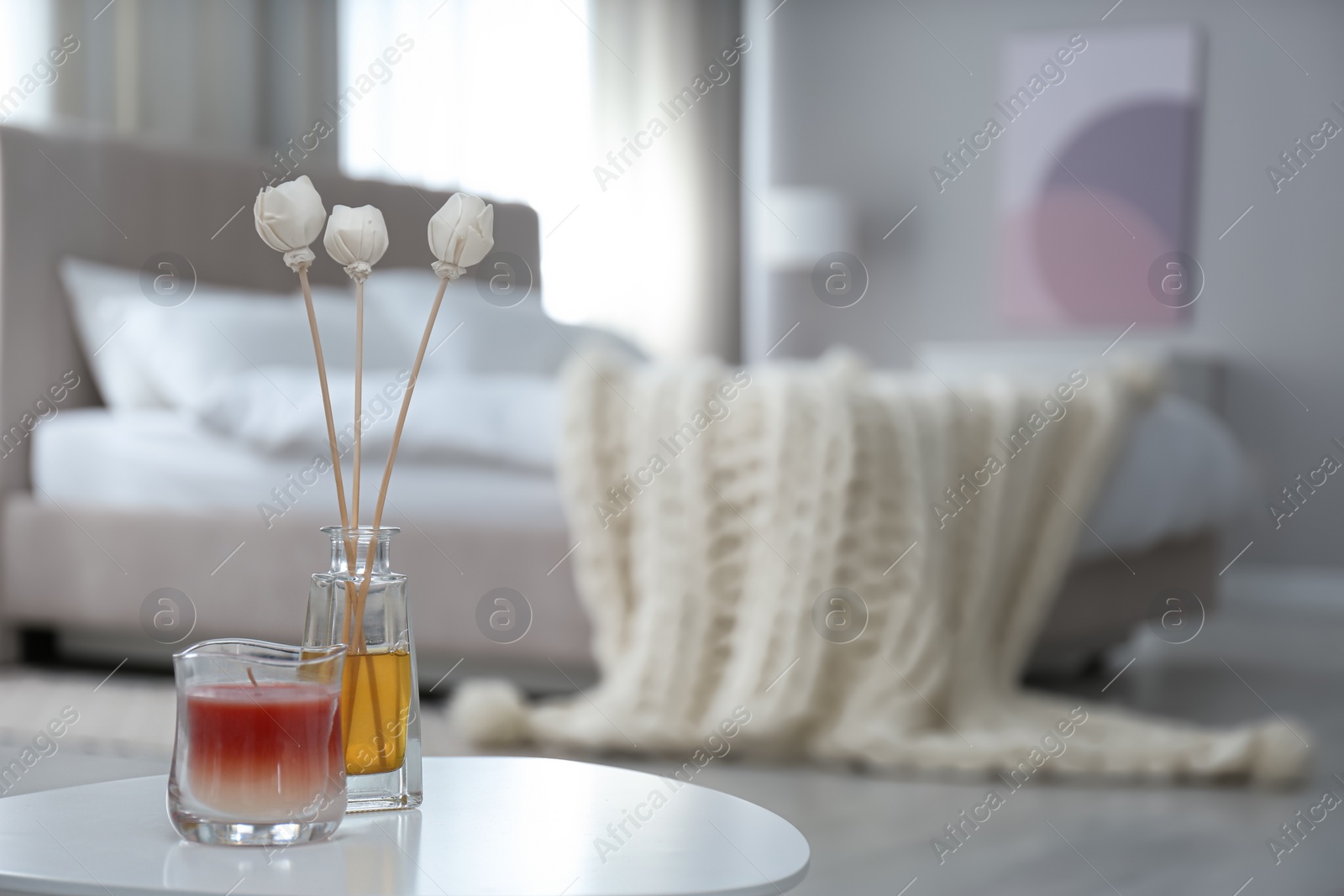 Photo of Air reed freshener and candle on white table in bedroom. Space for text