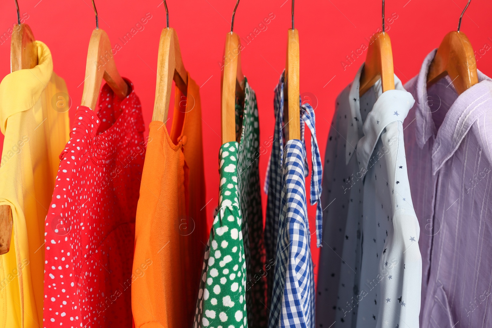 Photo of Bright clothes on hangers against red background, closeup. Rainbow colors