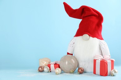 Photo of Cute Christmas gnome, gift boxes and festive balls on light blue background. Space for text