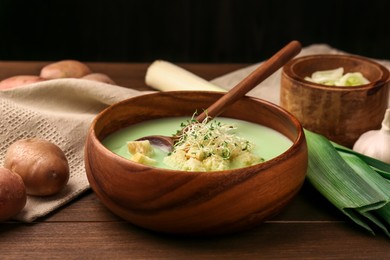 Photo of Bowl of tasty leek soup, spoon and ingredients on wooden table