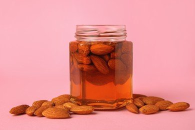 Photo of Jar with almonds and honey on pink background