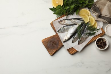 Fresh raw sprats, lemon and dill on white marble table, flat lay. Space for text