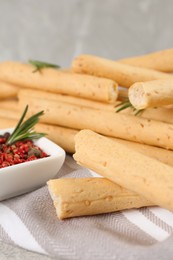 Photo of Tasty grissini with rosemary and pepper on napkin, closeup