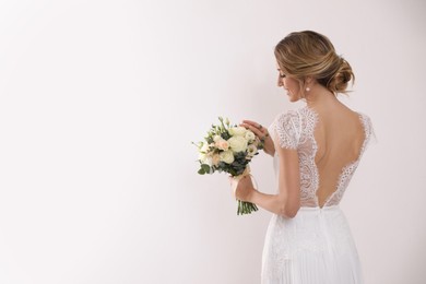 Photo of Young bride with elegant hairstyle holding wedding bouquet on white background, back view