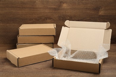 Closed and open cardboard boxes with bubble wrap on wooden table