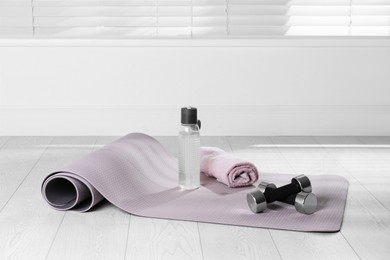 Photo of Exercise mat, dumbbells, towel and bottle of water on light wooden floor indoors