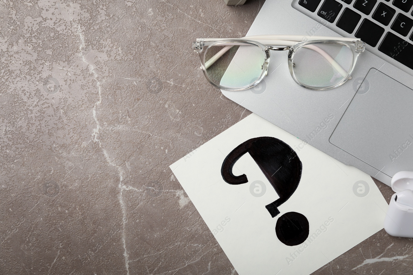 Photo of Notebook with question mark, laptop and eyeglasses on grey marble table, flat lay. Space for text