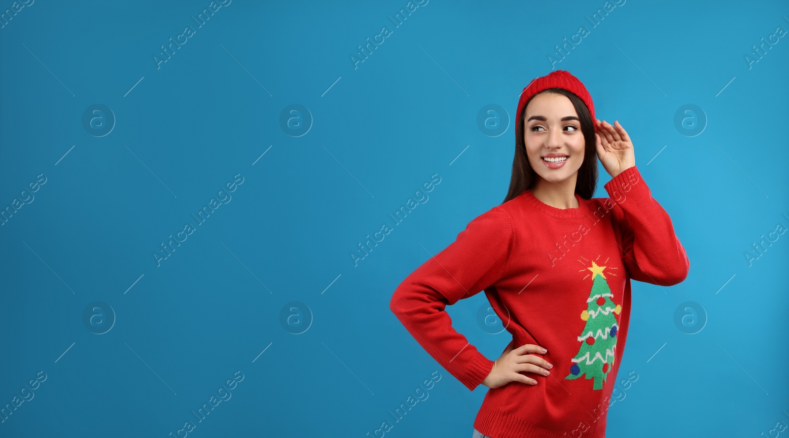 Photo of Young woman in Christmas sweater and hat on blue background, space for text