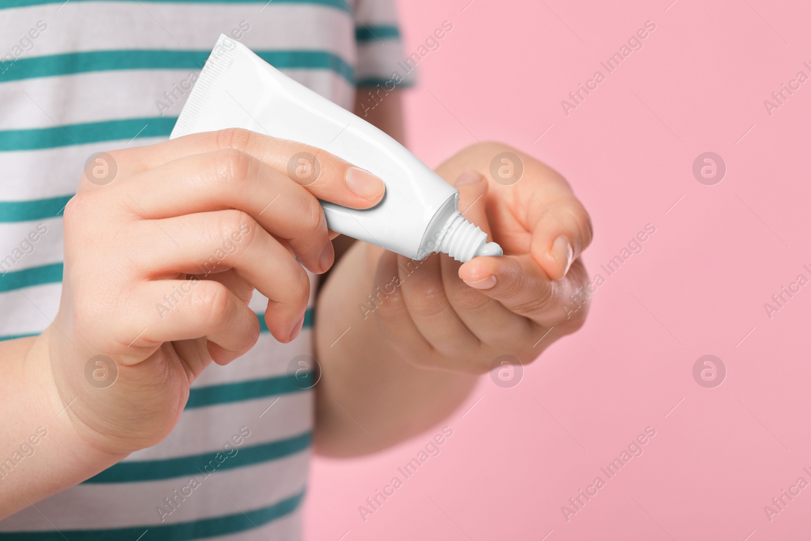 Photo of Woman applying ointment from tube onto her finger on pink background, closeup