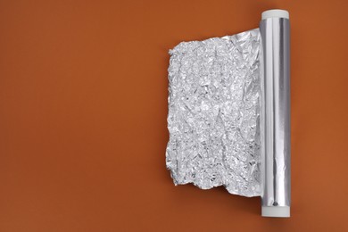 Photo of One roll of aluminum foil on brown background, top view. Space for text