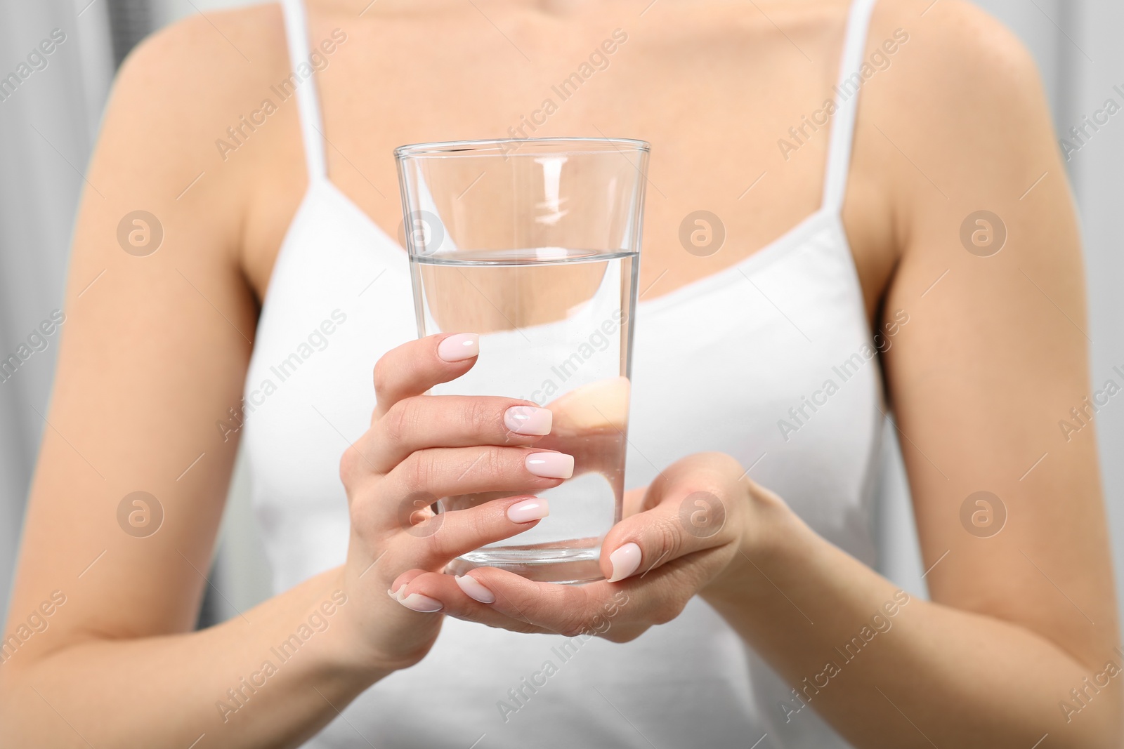 Photo of Healthy habit. Closeup of woman holding glass with fresh water indoors