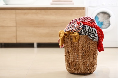 Photo of Wicker basket with dirty clothes on floor in bathroom. Space for text