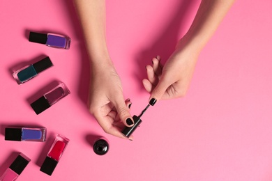 Woman applying nail polish on color background, top view