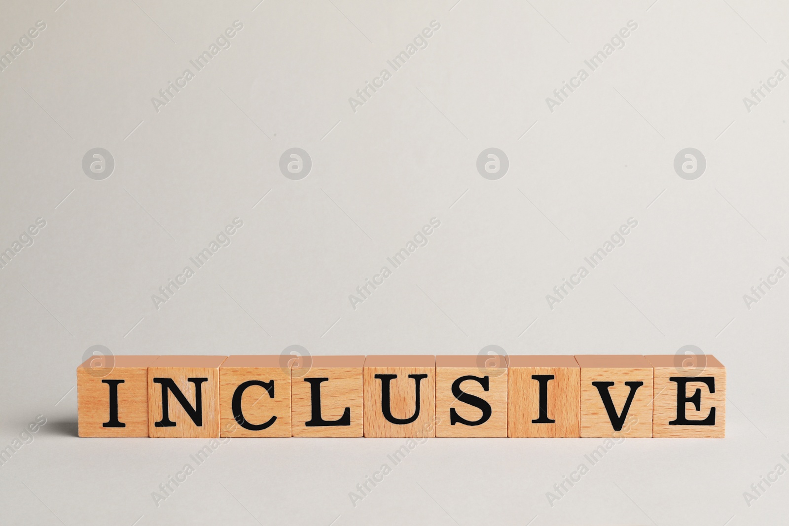 Photo of Wooden cubes with word Inclusive on beige background. Space for text