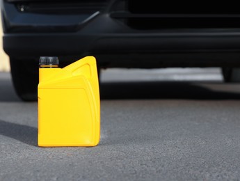 Yellow canister with motor oil near car on asphalt road