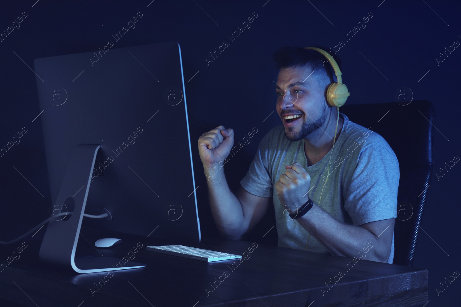 Photo of Happy man with headphones playing video game on modern computer in dark room