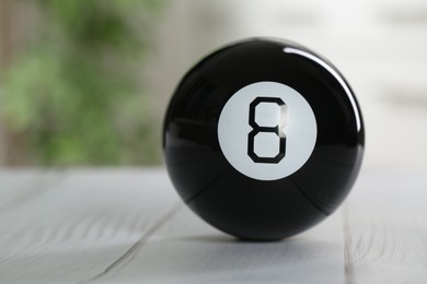 Magic eight ball on light wooden table, closeup. Space for text