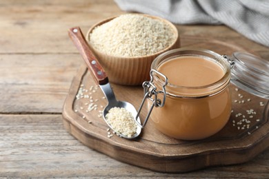 Jar of tasty sesame paste and seeds on wooden table