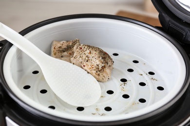 Delicious chicken with spices and spoon in multi cooker, closeup