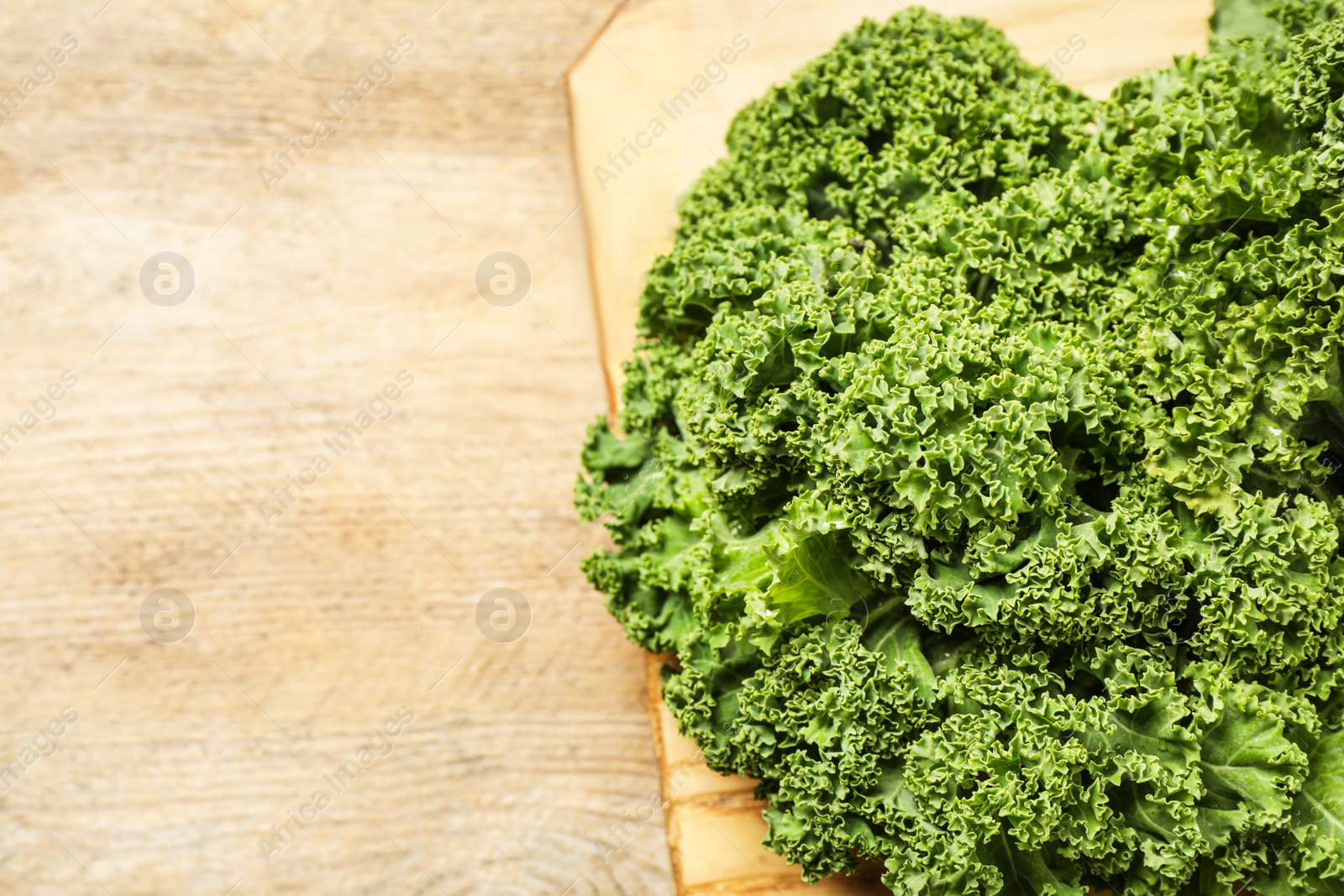 Photo of Fresh kale leaves on wooden table, closeup. Space for text