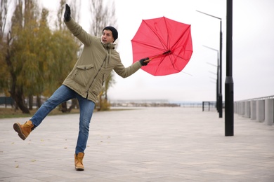 Photo of Man with red umbrella caught in gust of wind outdoors