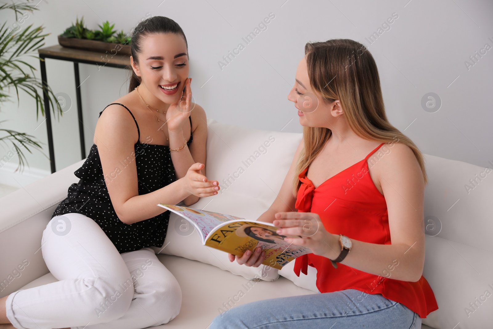 Photo of Happy women chatting about article in magazine on sofa indoors