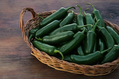 Photo of Wicker basket with green jalapeno peppers on wooden table, closeup