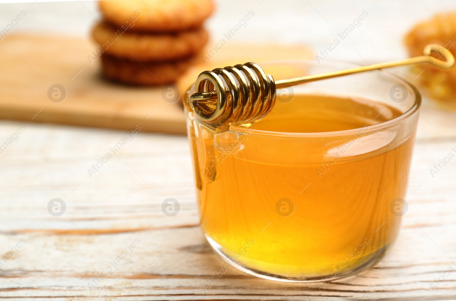 Photo of Tasty honey and metal dipper on white wooden table, closeup. Space for text