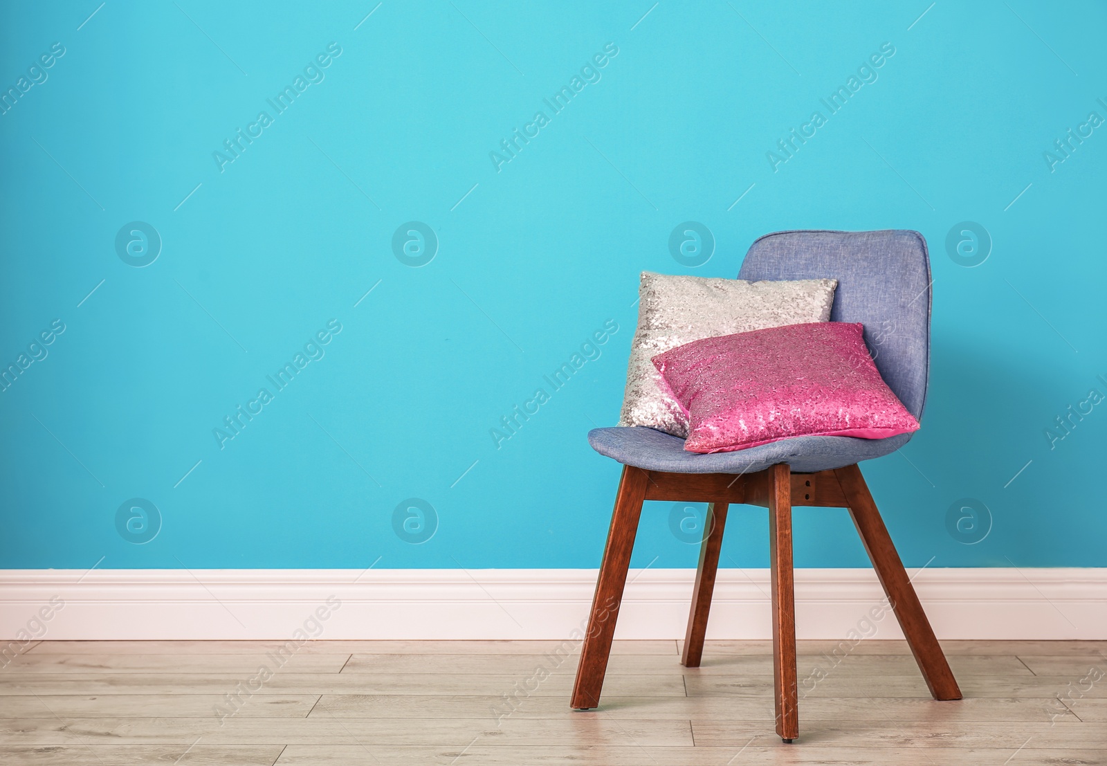 Photo of Different pillows on chair near color wall in room