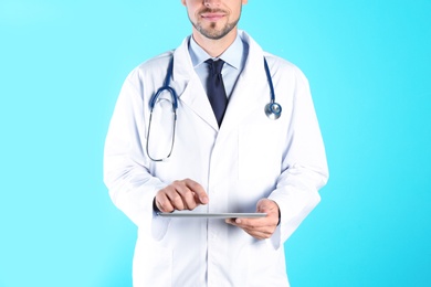 Male doctor holding modern tablet on color background, closeup