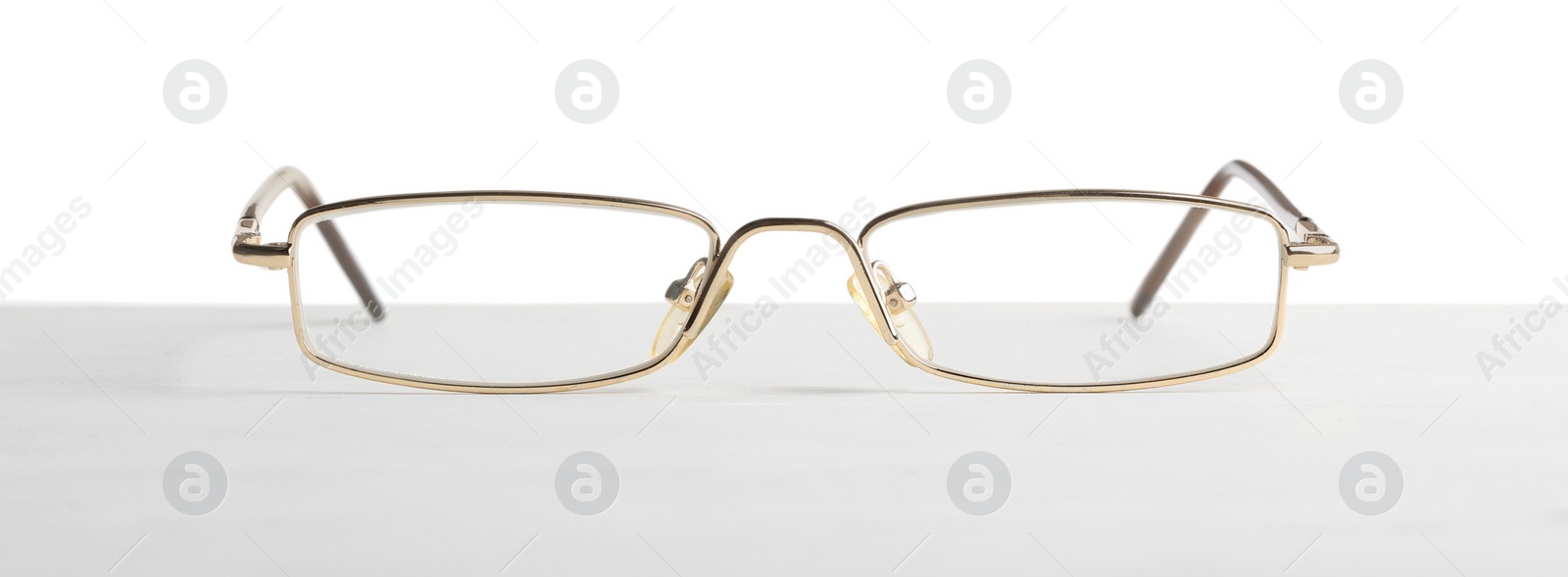 Photo of Stylish glasses with metal frame on table against white background