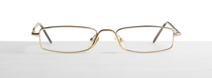 Stylish glasses with metal frame on table against white background