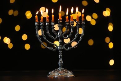 Photo of Silver menorah with burning candles against dark background and blurred festive lights. Hanukkah celebration