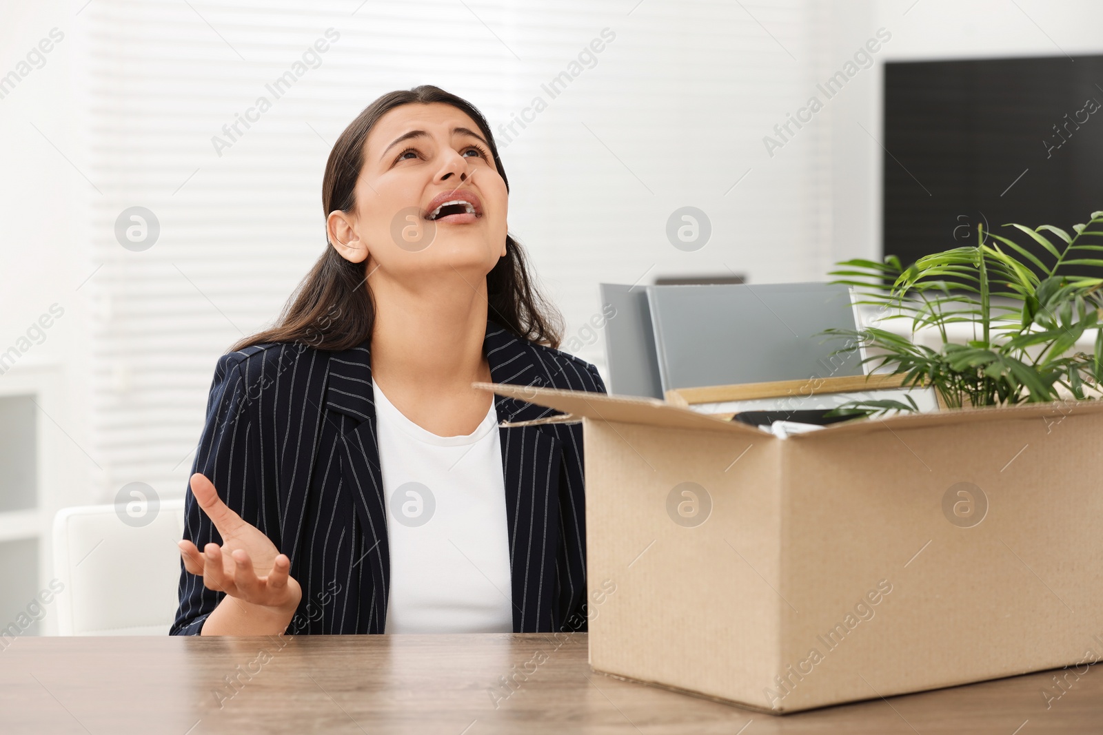 Photo of Unemployment problem. Woman with box of personal belongings at table in office