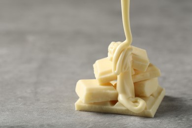 Photo of Pouring tasty white chocolate paste onto pieces on grey table, closeup. Space for text