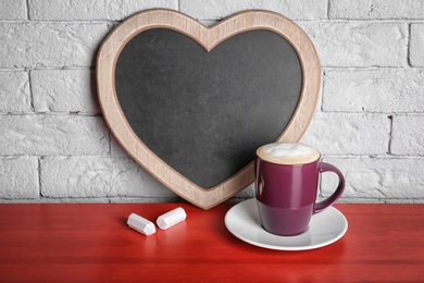 Photo of Cup of coffee on table near heart shaped chalkboard