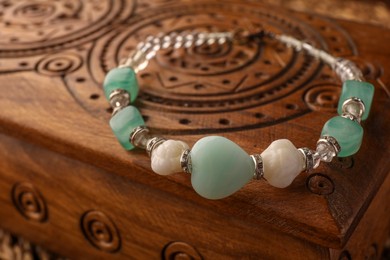 Photo of Beautiful bracelet with gemstones on wooden jewelry box, closeup